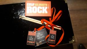 Accessoires du Rockstar Tour : baguettes de batteries, livre sur les objets cultes du rock, pass du groupe "La Pas Trop Matinale", CD du groupe "La Pas Trop Matinale". 