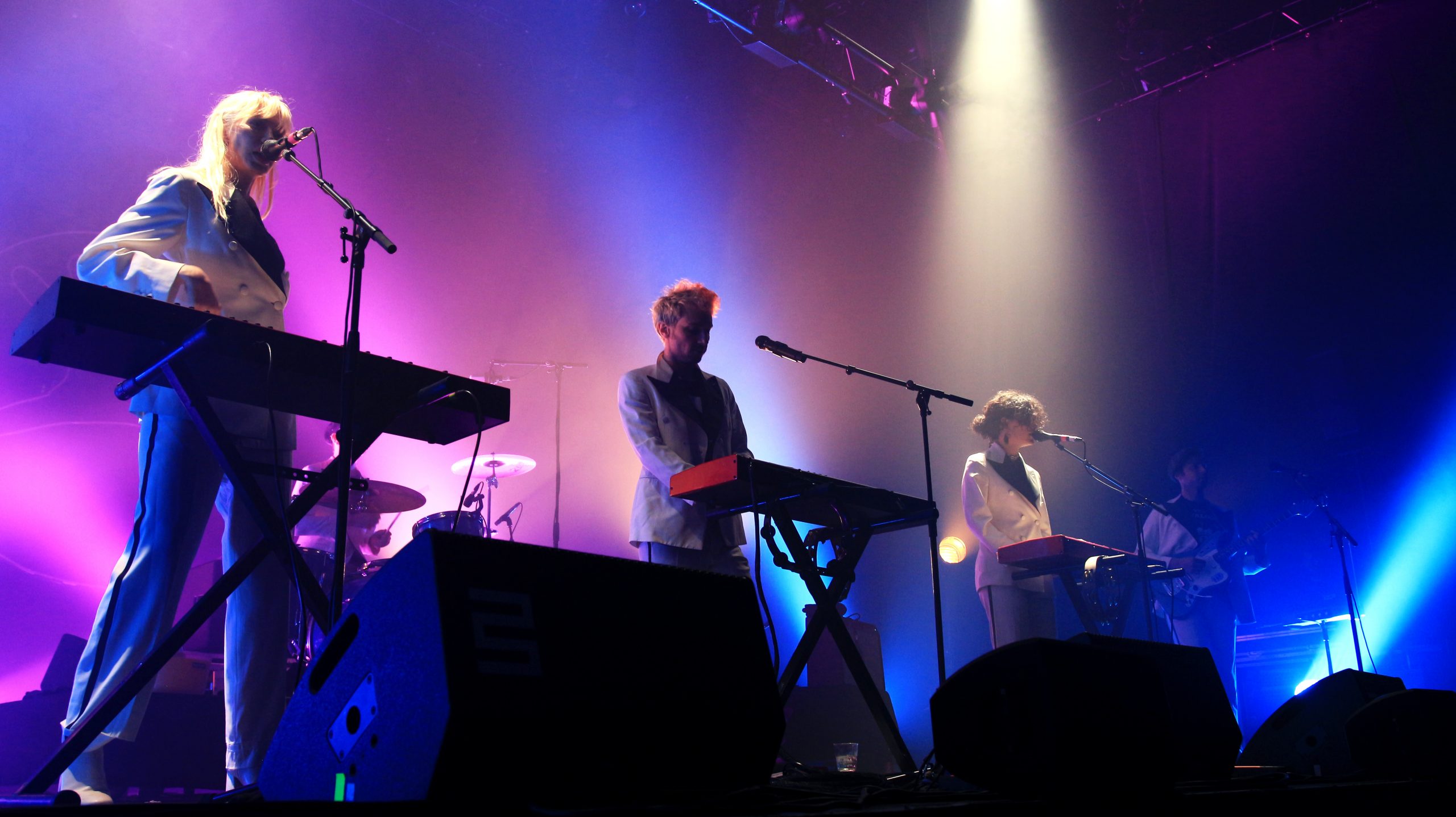 Quatre personnes sur une scène de concert. Trois claviers, une guitrare. En arrière plan une batterie. 